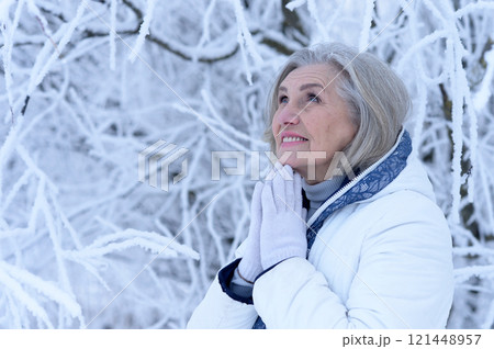 Beautiful elderly woman posing in a snowy winter park 121448957
