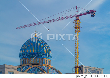 The process of building a mosque with decorated patterns and ornaments on vaults and dome of roof using a tower-type industrial construction crane. Exterior finishing Works. Lifting Heavy Loads 121449314