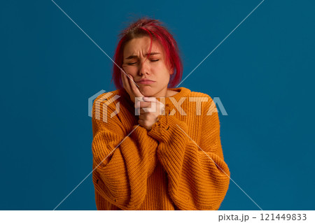 Woman with hand on chest, showing distress from respiratory problems or chest congestion against blue studio background. Woman with hand on chest, showing distress from respiratory problems or chest congestion against blue studio background. 121449833
