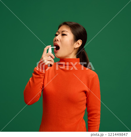 Woman using throat spray to ease pain and irritation caused by viruses or bacterial infections. Depicts home healthcare treatment for sore throat relief. 121449847