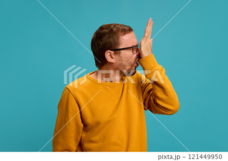 Young man dressed casual attire scratches his nose, suffers from allergies and rhinitis against blue studio background. Young man dressed casual attire scratches his nose, suffers from allergies and rhinitis against blue studio background. 121449950