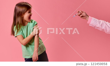 Girl in green shirt reacting dramatically holding hand on arm near syringe held out by doctor against pink studio background. Girl in green shirt reacting dramatically holding hand on arm near syringe held out by doctor against pink studio background. 121450058