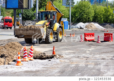 Construction crew works on road improvements in bright daylight near urban landscape. Copy space. Construction crew works on road improvements in bright daylight near urban landscape. Copy space. 121453530