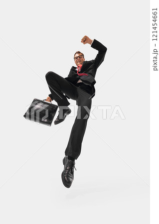 Business professional in black suit and red tie jumping energetically, raising fist and holding briefcase against white studio background. Business professional in black suit and red tie jumping energetically, raising fist and holding briefcase against white studio background. 121454661