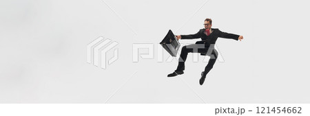 Banner. Businessman in black suit and red tie mid-air, holding black briefcase flying against white studio background with copy space. Banner. Businessman in black suit and red tie mid-air, holding black briefcase flying against white studio background with copy space. 121454662