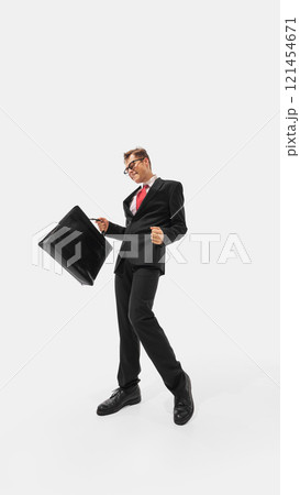 Man in sharp black suit and red tie striking exaggerated confident pose while holding briefcase in hand against white studio background. Man in sharp black suit and red tie striking exaggerated confident pose while holding briefcase in hand against white studio background. 121454671