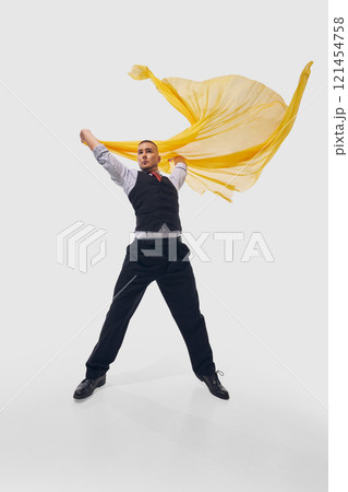Man lifts yellow fabric dramatically, dressed in formal black attire, creating commanding and expressive stance against white studio background. Man lifts yellow fabric dramatically, dressed in formal black attire, creating commanding and expressive stance against white studio background. 121454758