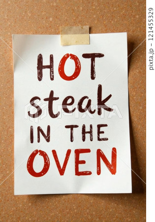 A sign is posted on a kitchen wall, alerting everyone that a hot steak is currently cooking in the oven. The colorful lettering emphasizes the dish's readiness for an enjoyable meal. 121455329
