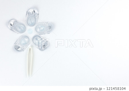 Top view of a creative flower consisting of containers for daily contact lenses, in the center there is a soft bluish lens, down like the stem of a plant there are tweezers for taking lenses on a 121458104