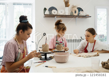Women and child engaged in pottery at a cozy studio during the day Women and child engaged in pottery at a cozy studio during the day 121458161