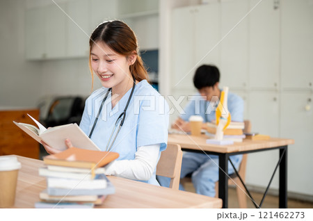 A smart and beautiful Asian female medical student in scrubs is reading or studying in the library. 121462273