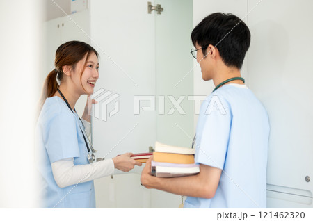 Two Asian male and female medical students are talking while getting their textbooks from a locker. Two Asian male and female medical students are talking while getting their textbooks from a locker. 121462320