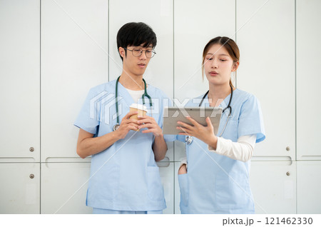 Two smart Asian doctors are discussing the medical cases on the screen in the locker room. Two smart Asian doctors are discussing the medical cases on the screen in the locker room. 121462330