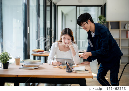 Two positive Asian college students are looking at a tablet screen and discussing. Two positive Asian college students are looking at a tablet screen and discussing. 121462358