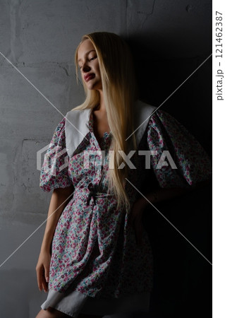 Woman in floral dress poses against a textured gray wall in dim lighting Woman in floral dress poses against a textured gray wall in dim lighting 121462387