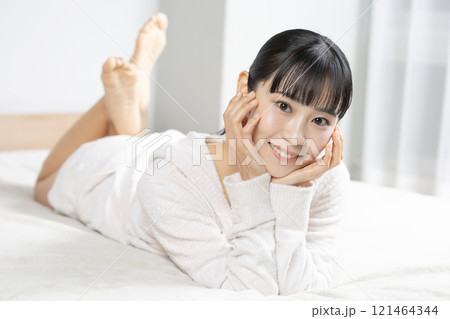 早朝ベッドの上にいるパジャマ姿の若い女性 121464344