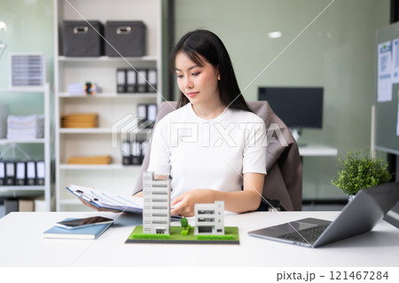 Young real estate agent worker working with laptop and tablet at table in office and small house beside it. Young real estate agent worker working with laptop and tablet at table in office and small house beside it. 121467284