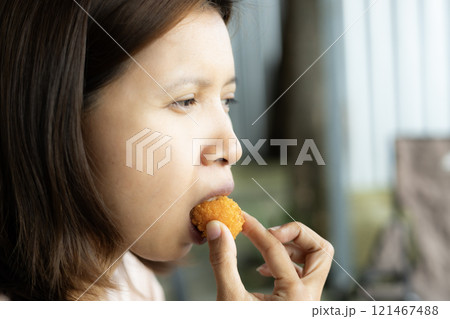 Woman bites into a crispy fried cheese ball. 121467488