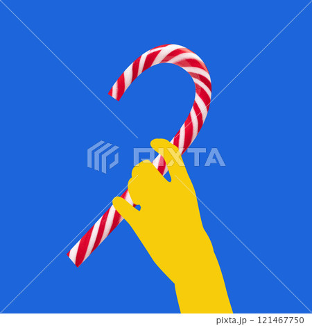 Contemporary art collage. Yellow hand holds candy cane against a bright blue background. Minimalist composition, bold colors. Festive and playful image. Contemporary art collage. Yellow hand holds candy cane against a bright blue background. Minimalist composition, bold colors. Festive and playful image. 121467750