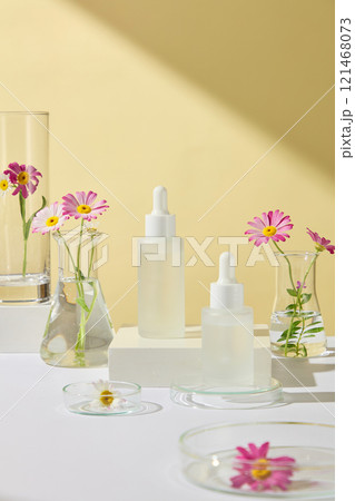 Chamomile flowers placed in some glassware and dropper bottles of serum mockup, displayed on a white surface, a yellow spa background. Advertising photo for cosmetics products. 121468073