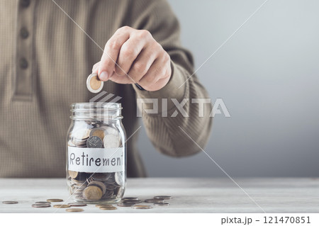 Man dropping a coin into a glass jar labeled 'Retirement,' symbolizing the commitment to saving and securing a future of financial stability. 121470851