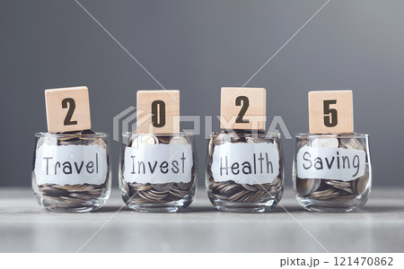 Glass jar filled with coins and 2025 write on wooden block, labeled Travel, Invest, Health and Saving, symbolizes diverse financial goals, growth, and a balanced approach to future Glass jar filled with coins and 2025 write on wooden block, labeled Travel, Invest, Health and Saving, symbolizes diverse financial goals, growth, and a balanced approach to future 121470862