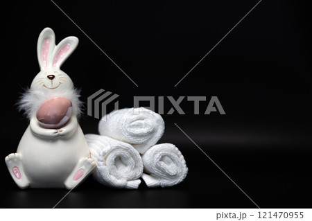 Easter white bunny with a brown egg on a black background with white spa towels Easter white bunny with a brown egg on a black background with white spa towels 121470955