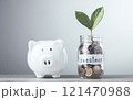 Glass jar filled with coins and a sprout labeled "Investment," placed next to a white piggy bank, Saving and investing for the future. Financial growth, long-term planning management strategies. Glass jar filled with coins and a sprout labeled "Investment," placed next to a white piggy bank, Saving and investing for the future. Financial growth, long-term planning management strategies. 121470988