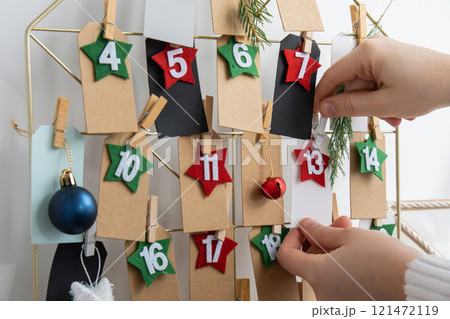 Number on craft paper notes with tasks before Christmas holidays. Female making kraft paper for handmade advent calendar Made with your own hands step by step DIY 121472119