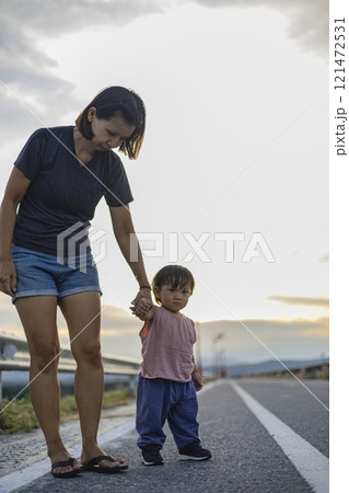 Mother and her toddler are standing on a road. Mother and her toddler are standing on a road. 121472531