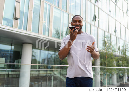 African american man talking on smartphone on street in city outdoor. Man with cell phone chatting with friends. Smiling person making answering call by cellphone. Guy having conversation by mobile 121475160