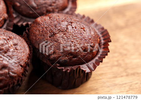 Freshly baked chocolate muffins in brown paper wrappers on a wooden surface. Concept of homemade treats and sweet indulgence 121478779