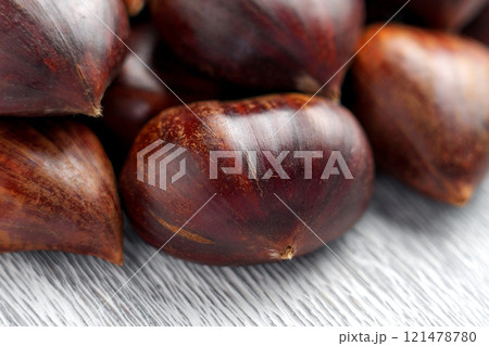 Group of fresh whole chestnuts with glossy nut shells arranged on a gray textured surface. Close up 121478780
