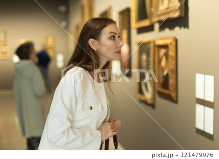 Woman examines a painting in detail in a museum Woman examines a painting in detail in a museum 121479976