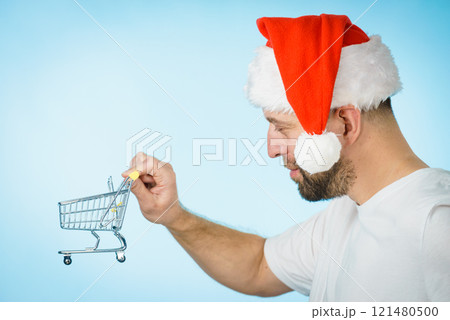 Man in santa hat holds empty shopping cart Man in santa hat holds empty shopping cart 121480500
