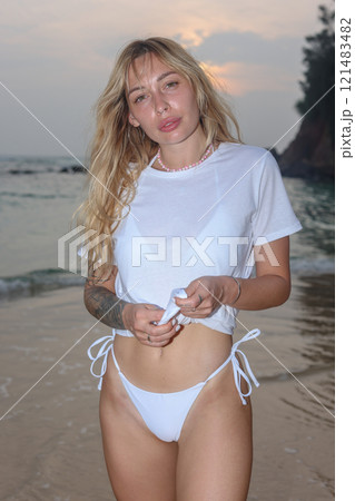 A Woman Dressed in Elegant White Swimwear Embracing the Beauty of Sunset Beach Serenity 121483482