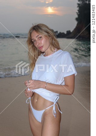 A Woman Dressed in Elegant White Swimwear Embracing the Beauty of Sunset Beach Serenity 121483485