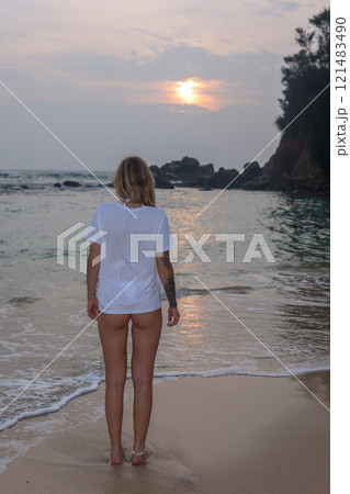 A stylish woman in a white tee shirt enjoys a vibrant sunset at the beach, soaking in the moment A stylish woman in a white tee shirt enjoys a vibrant sunset at the beach, soaking in the moment 121483490