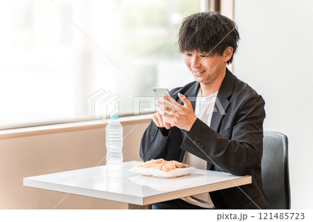 食堂・カフェでランチを食べながらスマホを見るビジネスマン・男性 食堂・カフェでランチを食べながらスマホを見るビジネスマン・男性 121485723