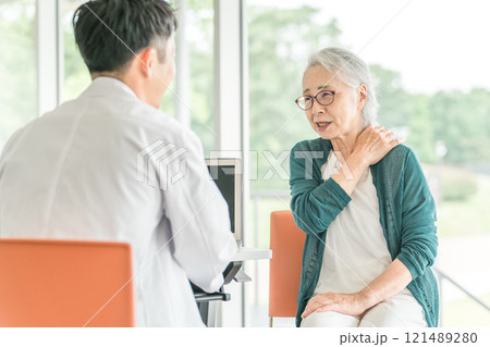 肩こり・肩を痛がるシニア女性と診察する男性医師の後ろ姿 121489280