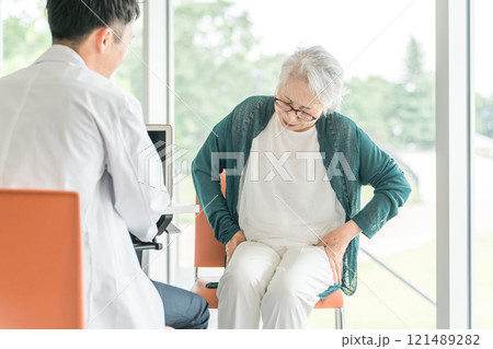 骨盤の痛みを訴えるシニア女性と診察する男性医師の後ろ姿 121489282