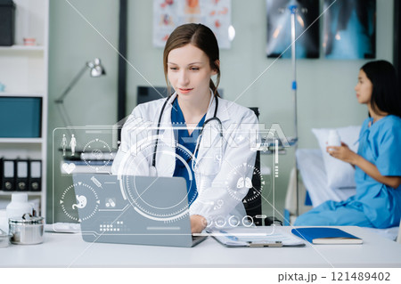 Young female doctor in white medical uniform using laptop and tablet talking video conference call at desk,Doctor sitting at desk 121489402
