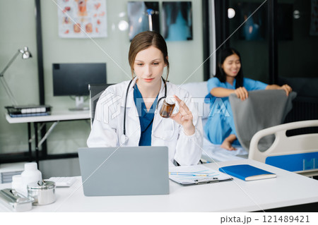 Young female doctor in white medical uniform using laptop and tablet talking video conference call at desk,Doctor sitting at desk 121489421