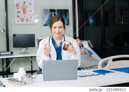 Young female doctor in white medical uniform using laptop and tablet talking video conference call at desk,Doctor sitting at desk 121489422
