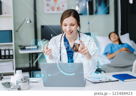 Young female doctor in white medical uniform using laptop and tablet talking video conference call at desk,Doctor sitting at desk 121489423