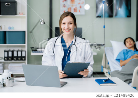 Young female doctor in white medical uniform using laptop and tablet talking video conference call at desk,Doctor sitting at desk 121489426