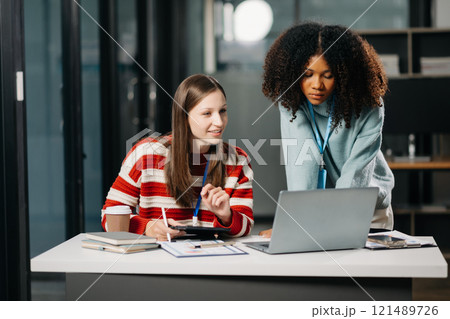 Businesswomen work and discuss their business plans. African women employee explains and shows her colleague the results paper in modern office. 121489726