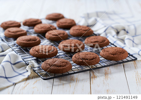 Freshly baked chocolate brownie cookies cooling on a black wire rack, with in a light kitchen table, selective focus. 121491149