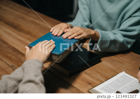 Group of Christians sit together and pray around a wooden table with blurred open Bible pages in their homeroom. Prayer for brothers, faith, hope, a Group of Christians sit together and pray around a wooden table with blurred open Bible pages in their homeroom. Prayer for brothers, faith, hope, a 121491327