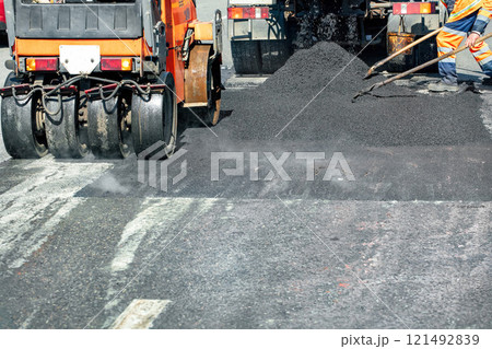 Road workers expertly laying new asphalt on a sunny day in an urban area 121492839